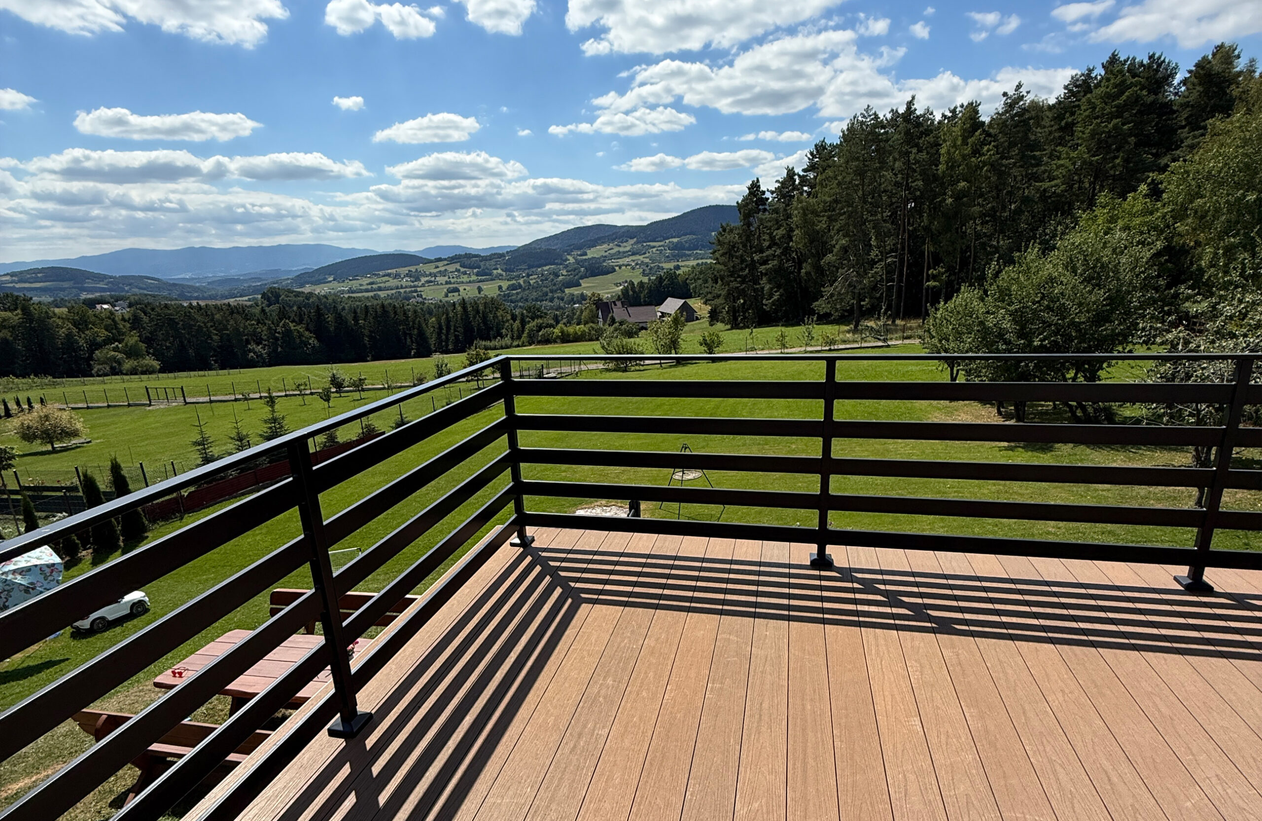 Elevated balcony view of a terrace with composite decking and a table overlooking a valley