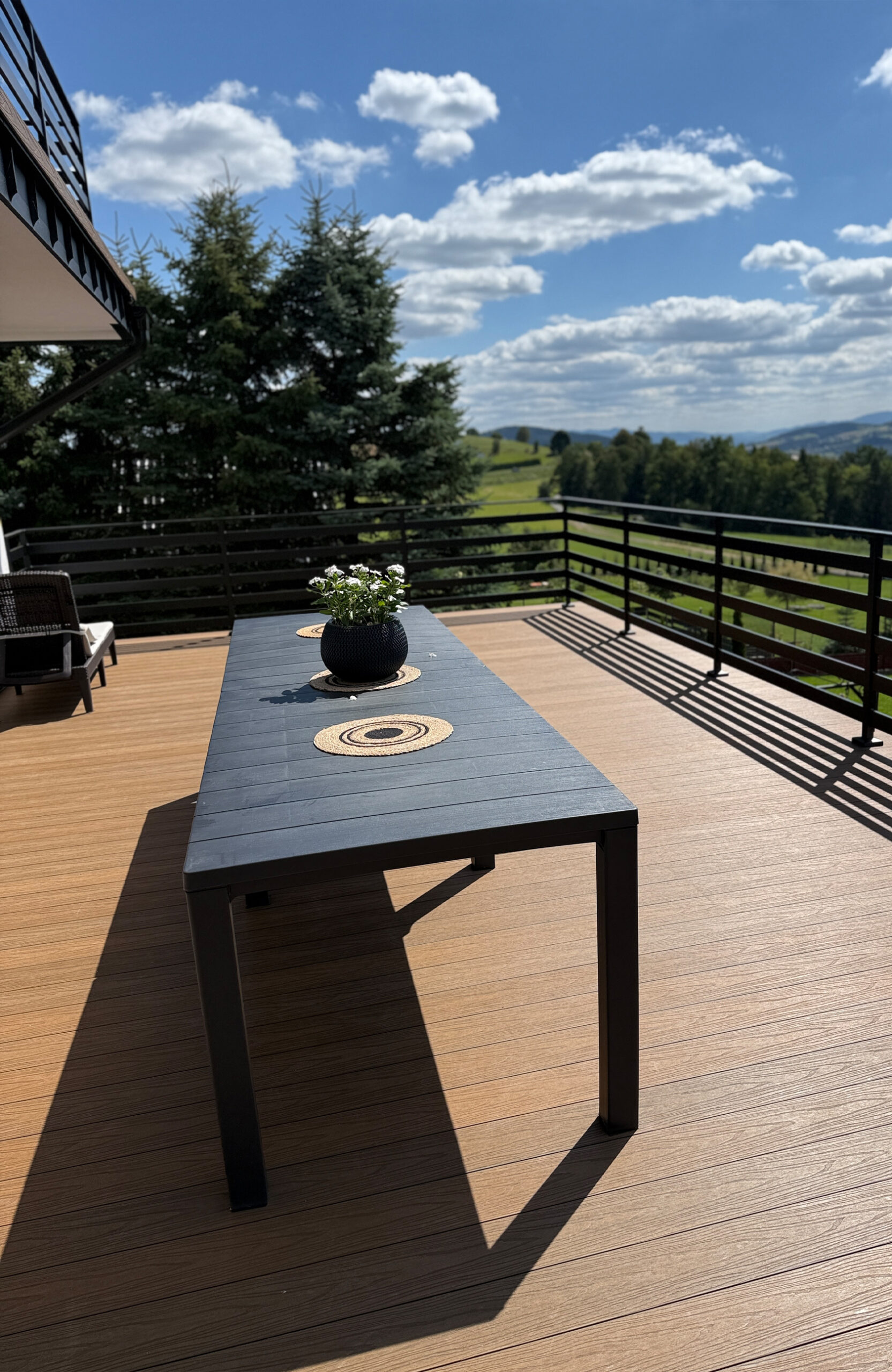 Close-up of a composite wood deck with a table and a view of rolling green hills.