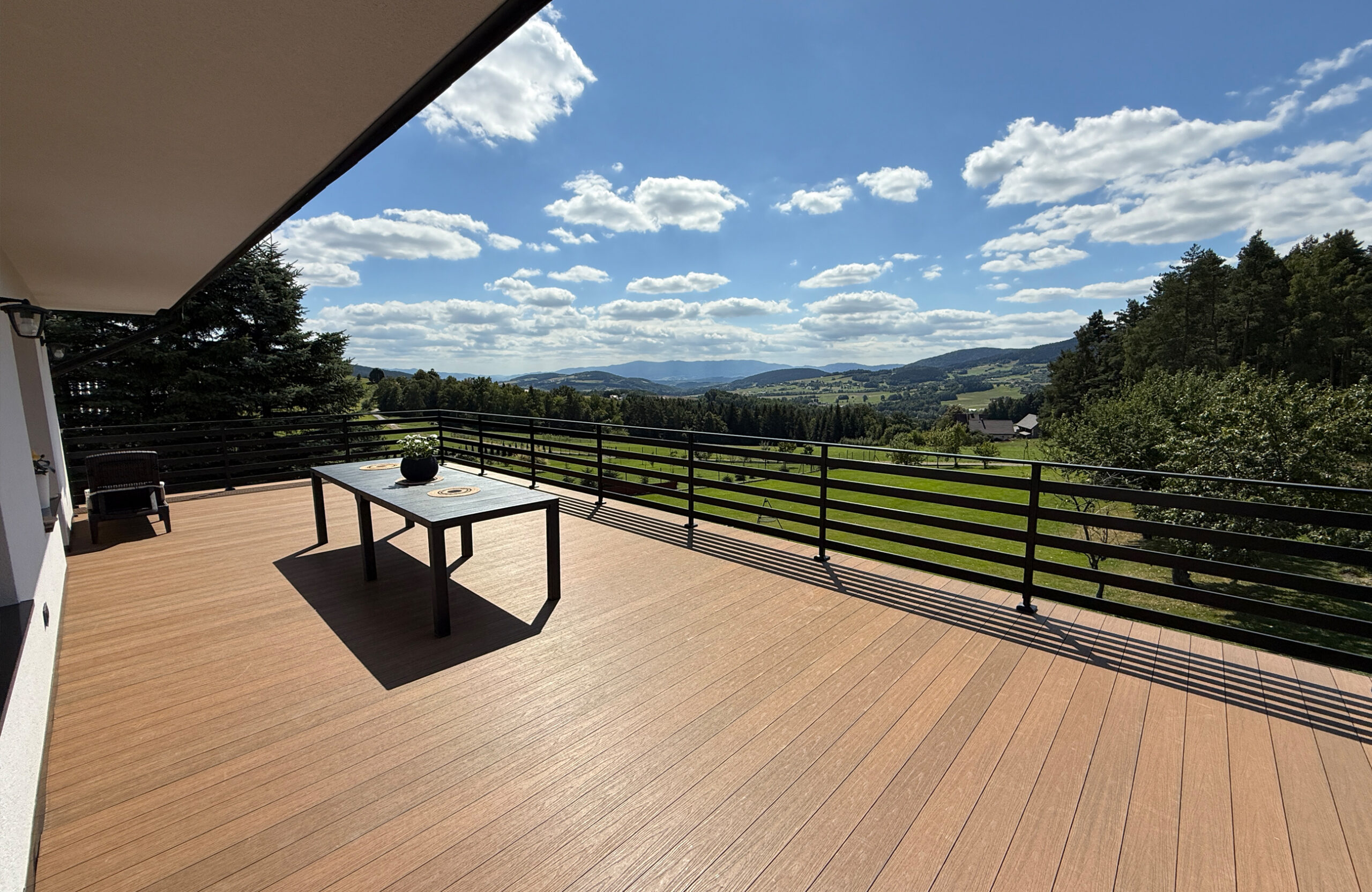 Low-maintenance composite decking creates a modern and functional outdoor living space, featuring a cozy seating area with a table, plant, and spectacular mountain views.