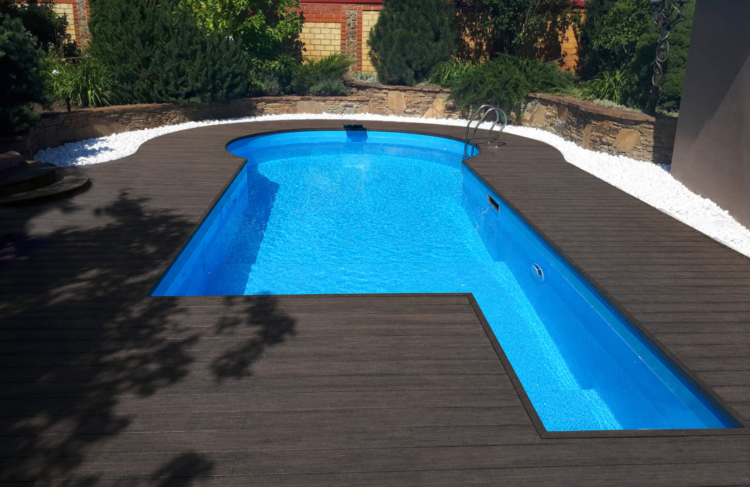 Outdoor swimming pool surrounded by walnut composite decking and landscaped garden
