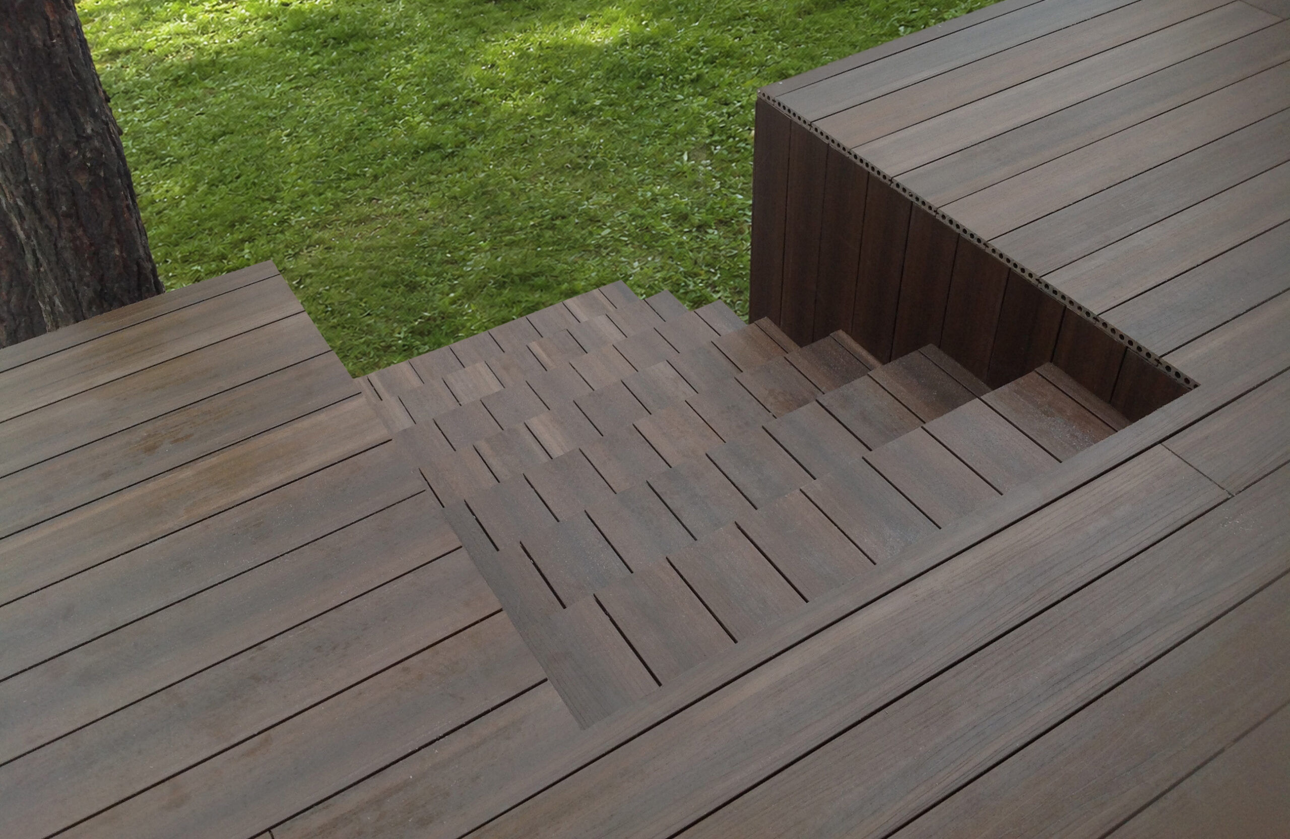 An angled overhead shot showing a walnut-colored composite deck featuring integrated steps, set beside a grassy lawn and a tree trunk
