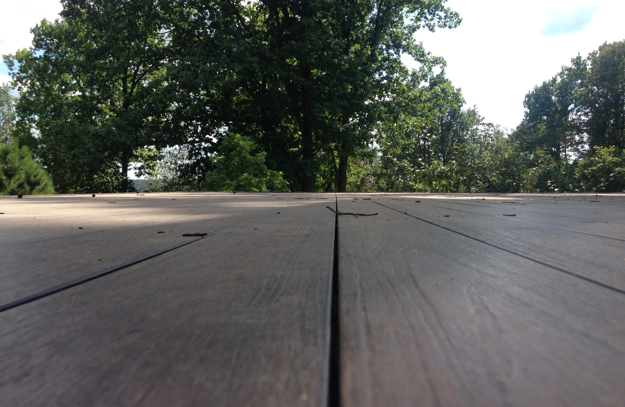 Close-up view of LEGRO walnut composite decking surrounded by trees