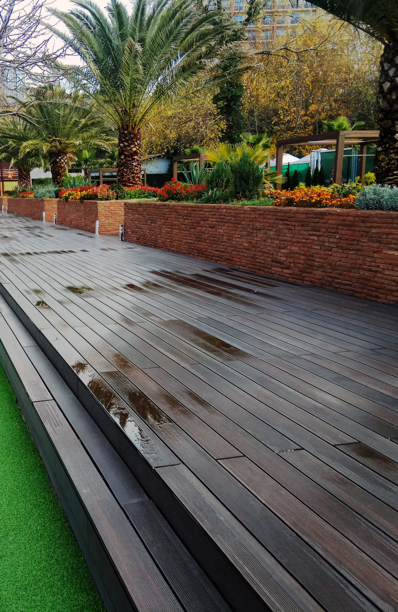 LEGRO walnut composite decking in a landscaped outdoor area with palm trees and garden beds
