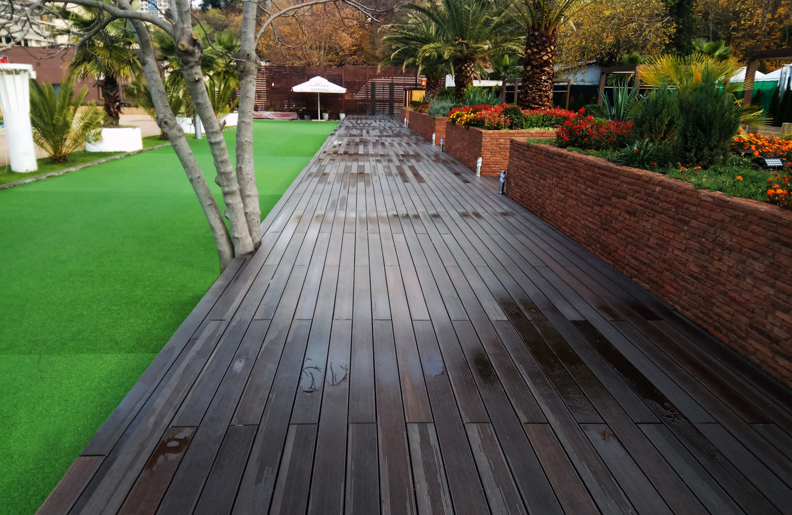 LEGRO walnut composite decking in a landscaped outdoor area with palm trees and garden beds