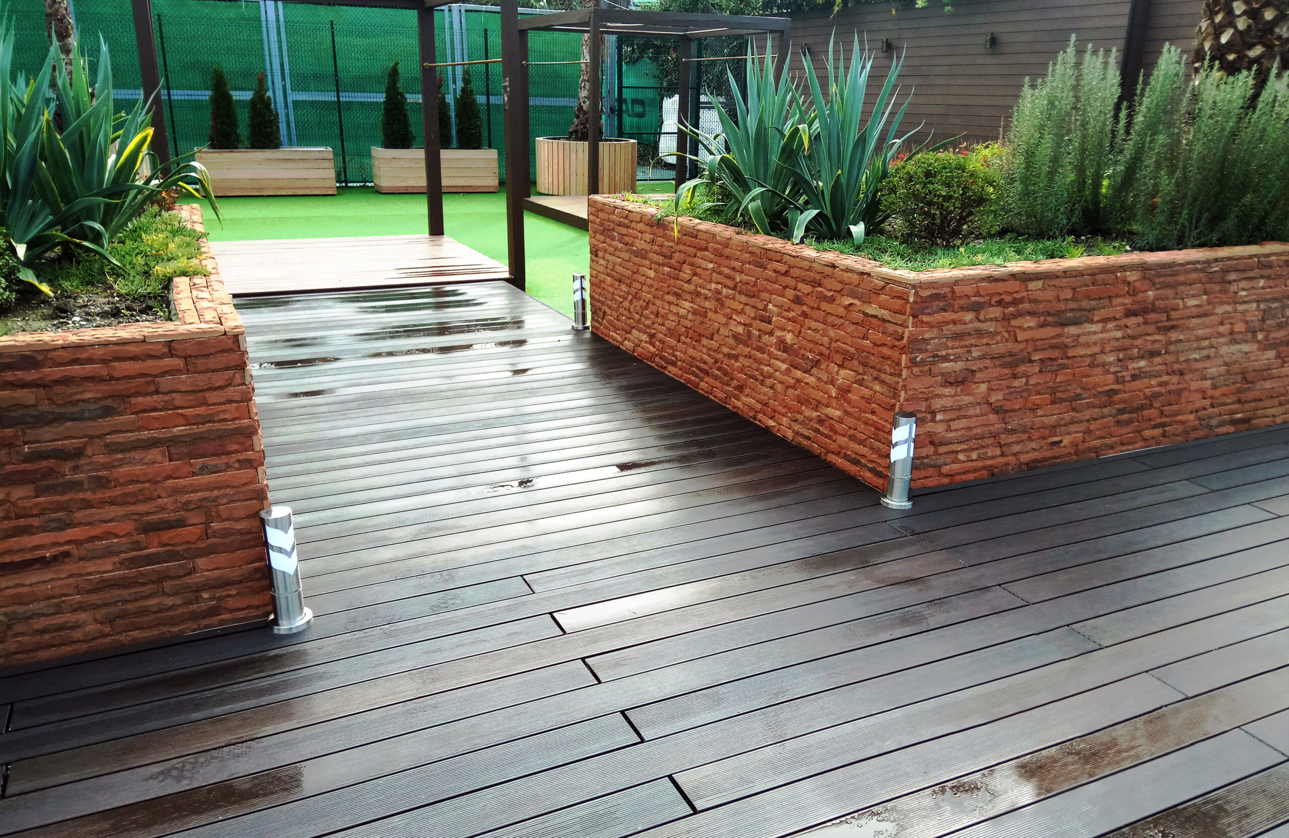 LEGRO walnut composite decking walkway between raised garden beds in a landscaped outdoor area