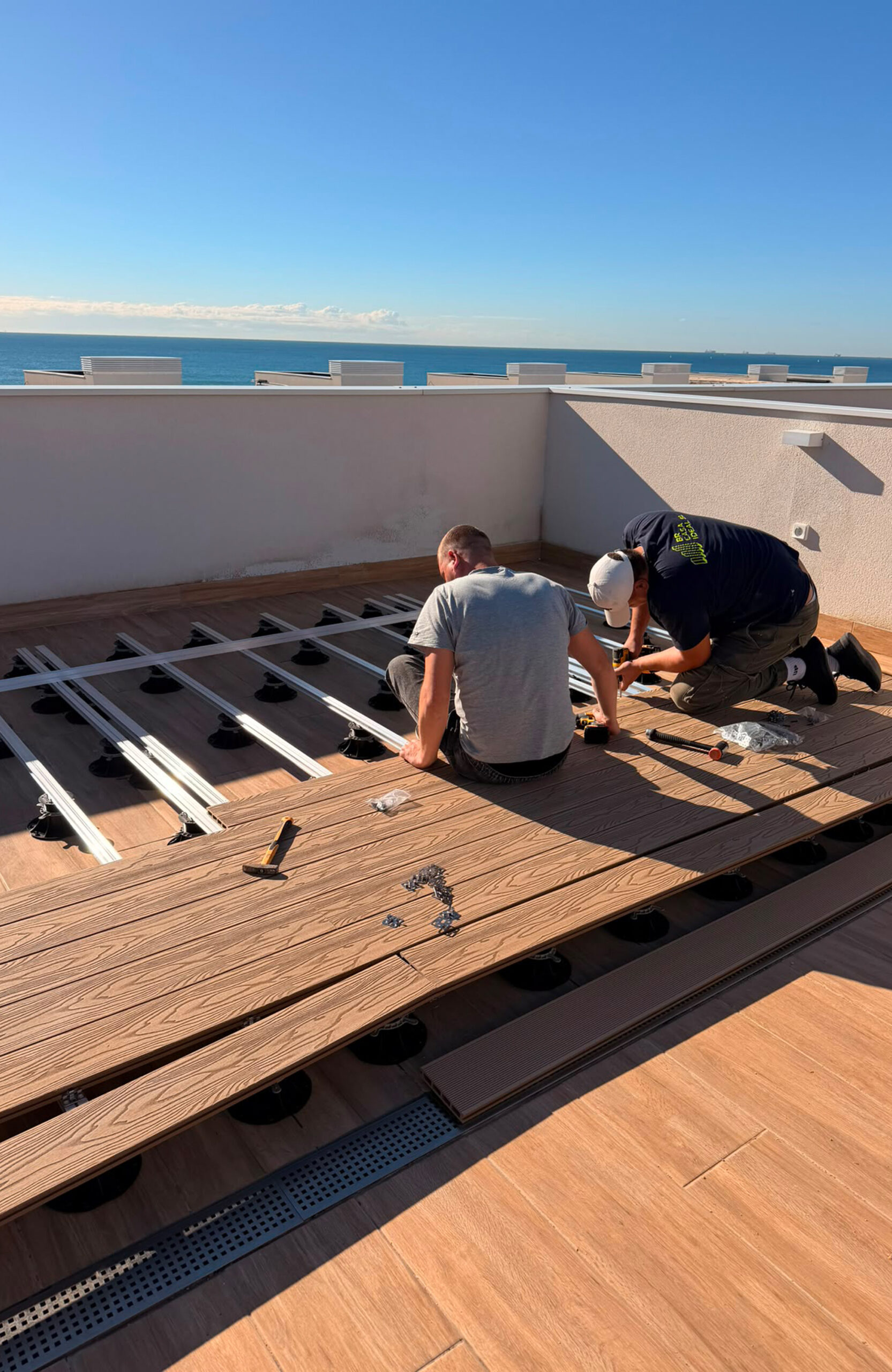 Two installers secure Bruggan Elegant Copper Natural decking boards onto an aluminum substructure