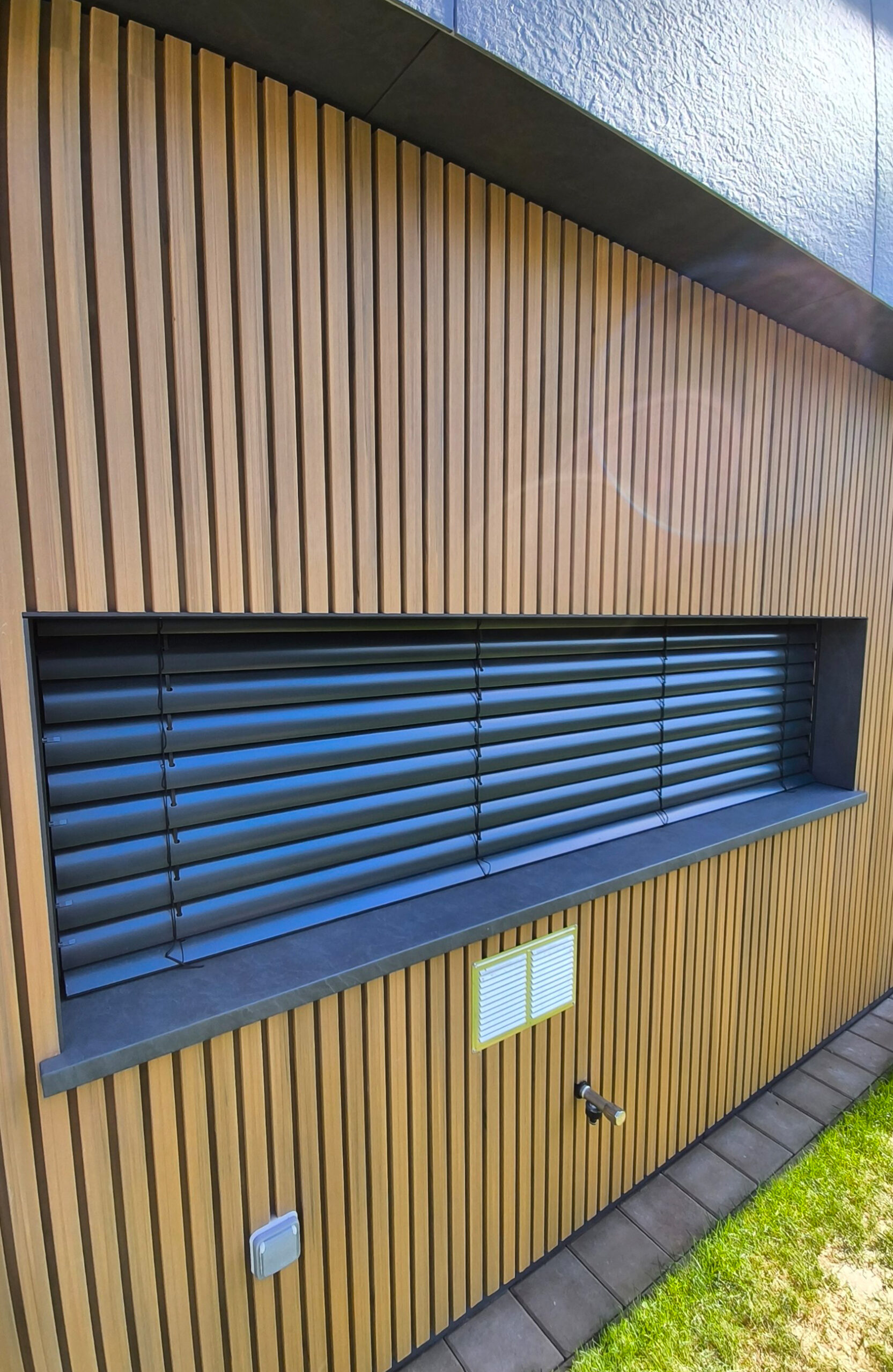 Close-up of LEGRO FS15 Maple WPC facade cladding with vertical wood-look slats around a window in Bratislava